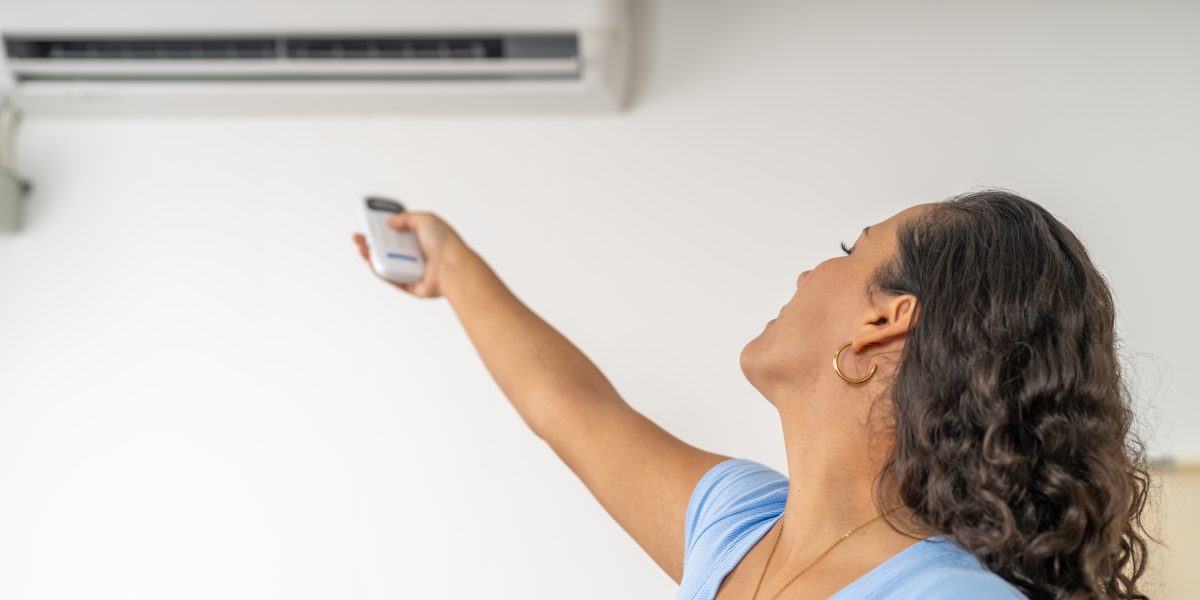 A woman, feeling the heat, reaches up to activate her air conditioner with a remote control for a cool environment.