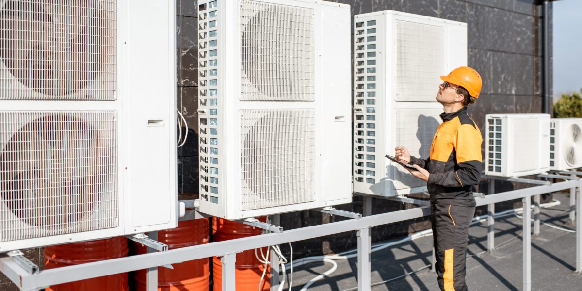 Professional workman in protective clothing adjusting the outdoor unit of the air conditioner or heat pump with digital tablet